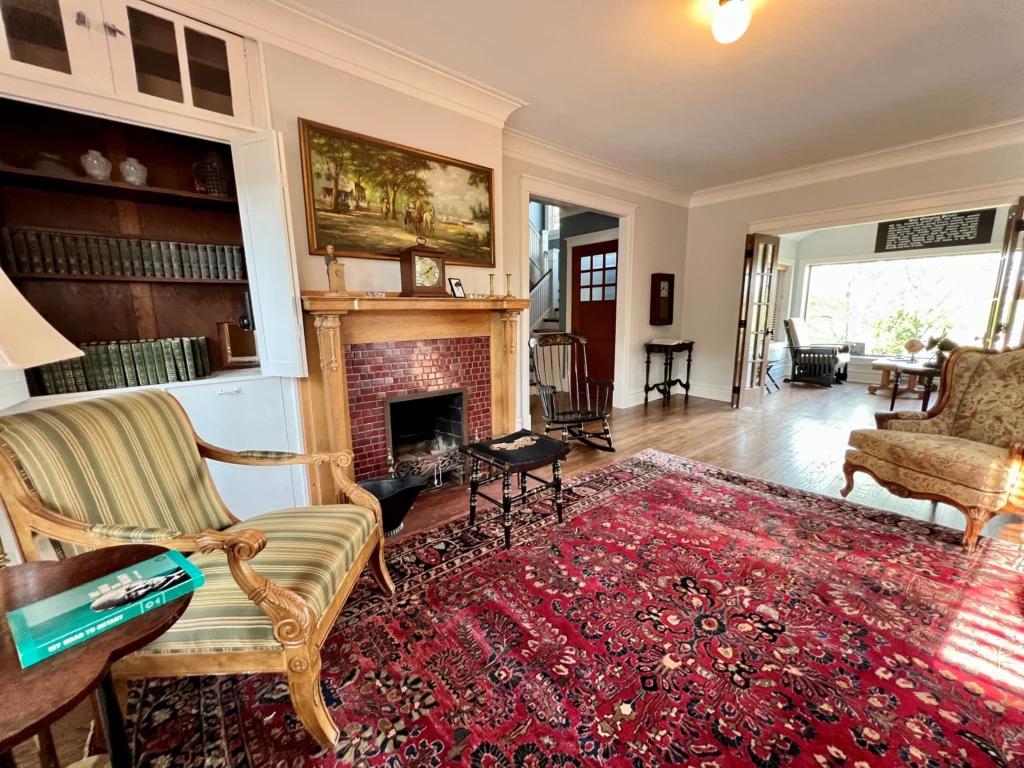 Restored fireplace room with period furniture, rugs, and adjoining sun porch.
