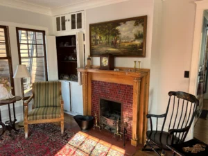 Restored fireplace room with period chairs, rug, and built-in shelving.