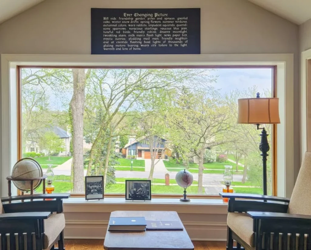 Front Sun Porch – Spring View Restored sun porch with chairs and a table facing a large window and spring greenery.