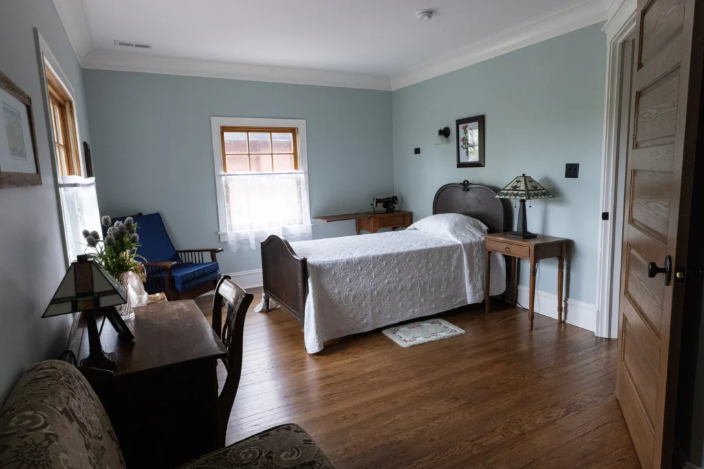 Guest Bedroom Interior – View 2 Guest bedroom with two beds, wood floors, windows, and period furnishings.