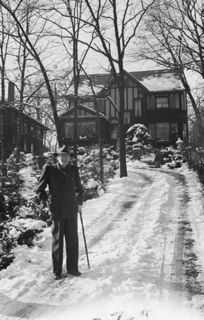 Historic black-and-white winter view of the Harris Home with a person standing along the snowy drive.